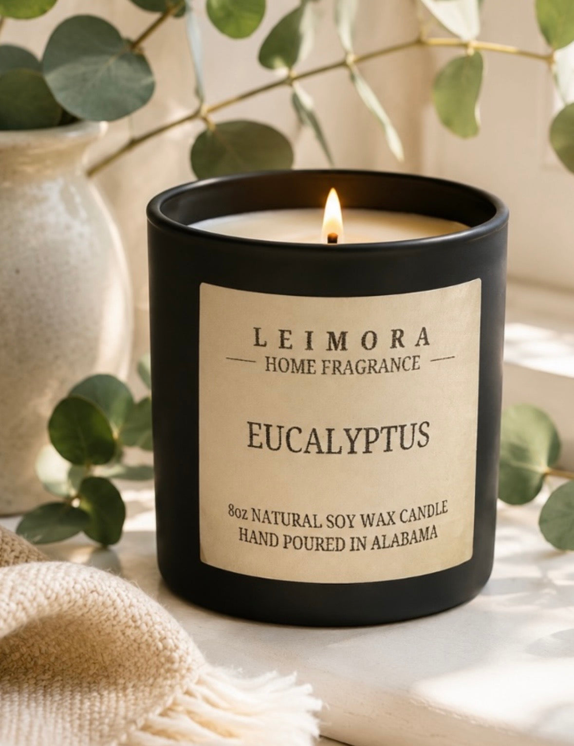 Eucalyptus lit soy candle in a black vessel neat green leaf plant.